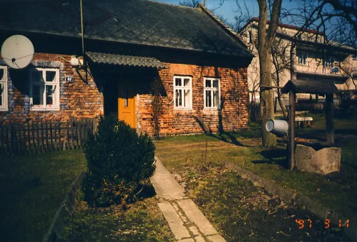 Stary murowany dom kryty dachówką, otoczony drzewami.