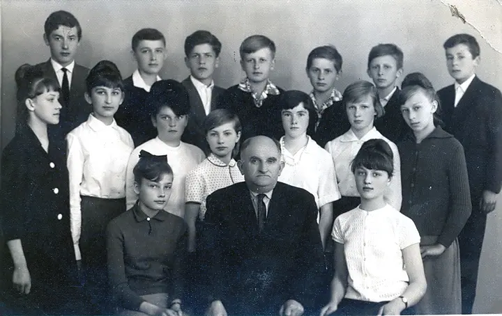 Czarno-białe zdjęcie klasowe z nauczycielem siedzącym pośrodku.