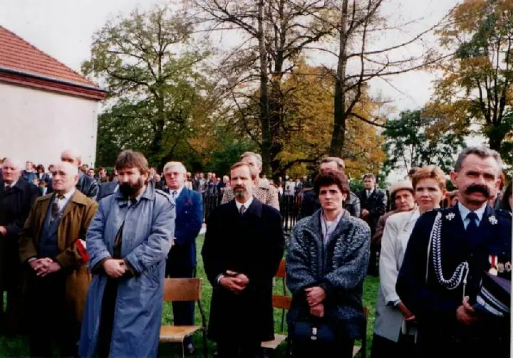 Uroczystość przed budynkiem szkoły: poczty sztandarowe, flagi biało-czerwone, mieszkańcy i kombatanci.