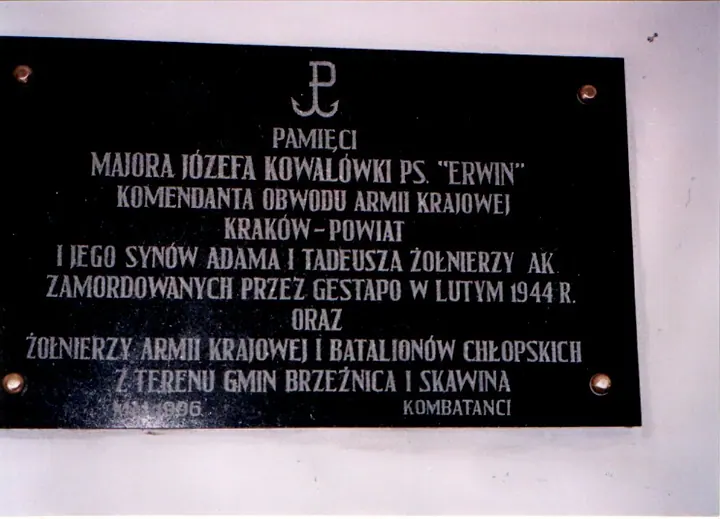 Czarna tablica pamiątkowa ze znakiem Polski Walczącej i wykutym napisem.