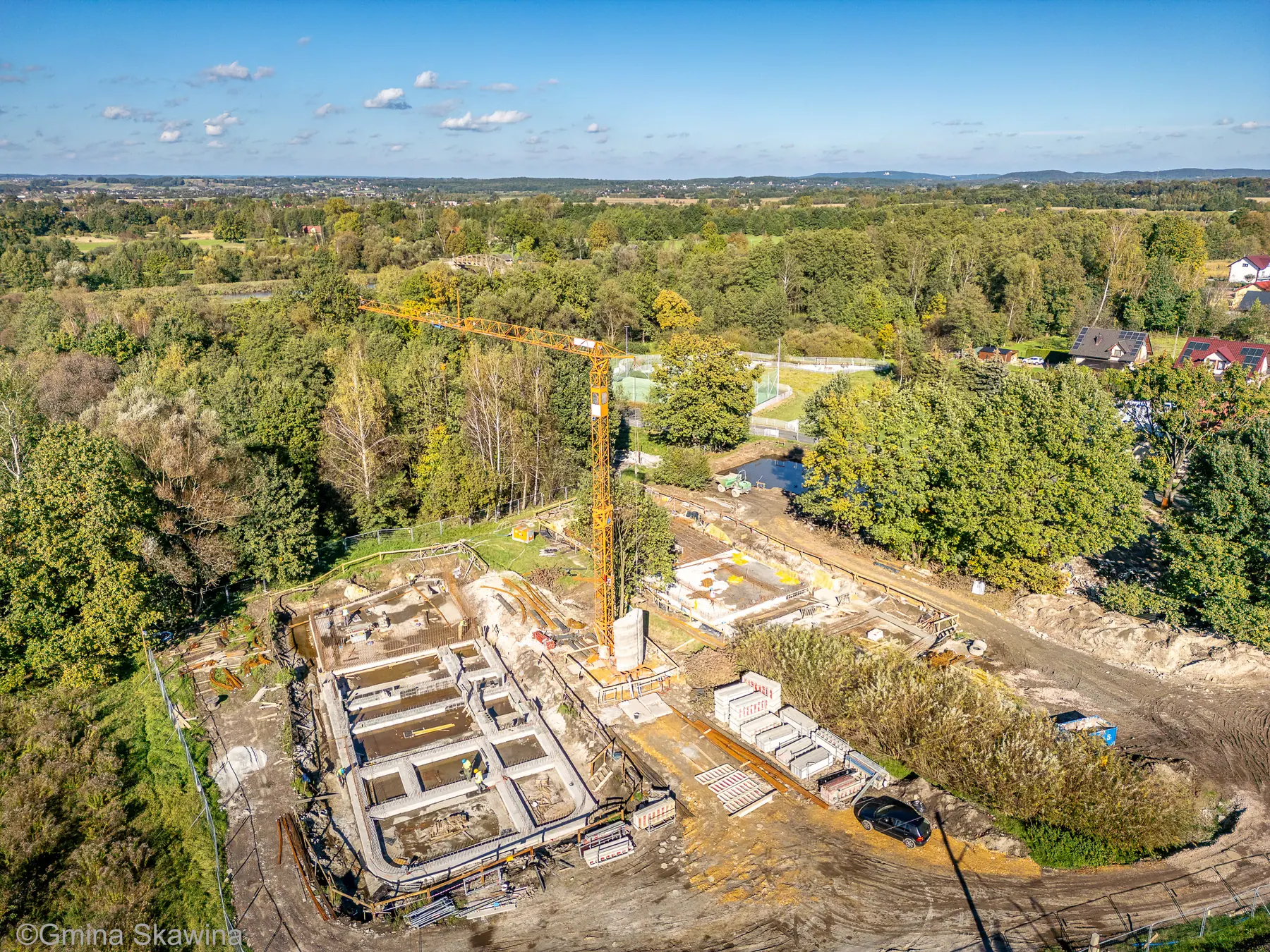Betonowe fundamenty tworzące obrys budynków, obok żuraw i zaplecze budowy.