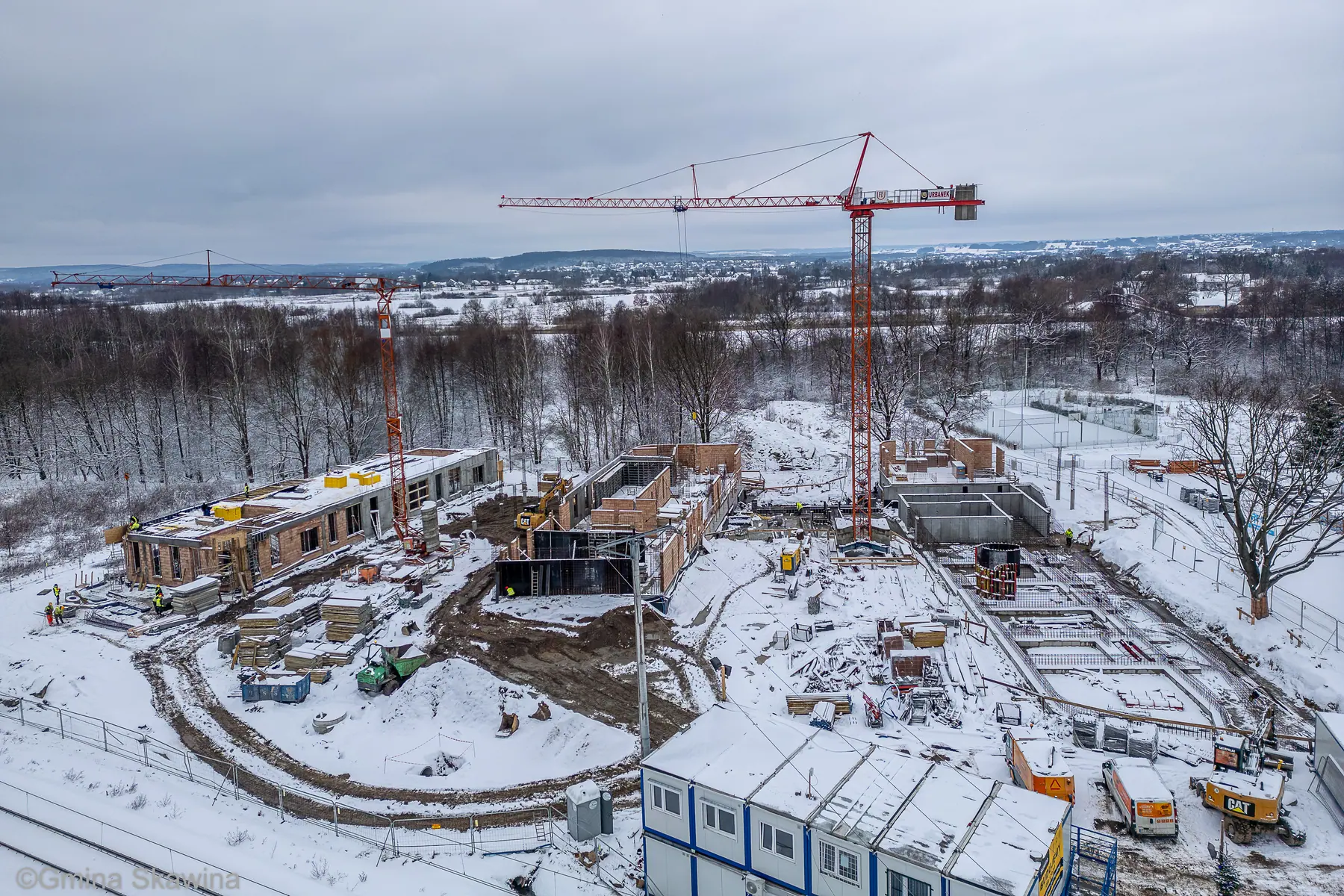 Ośnieżony plac budowy, dwa żurawie, wznoszone ściany parteru.