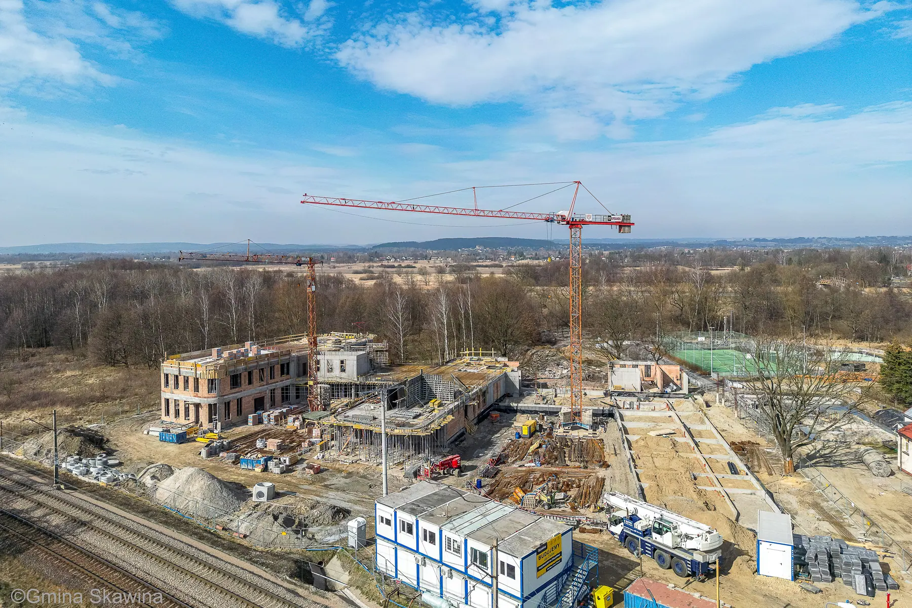 Ceglane ściany dwóch kondygnacji szkoły, dwa żurawie wieżowe, błękitne niebo.