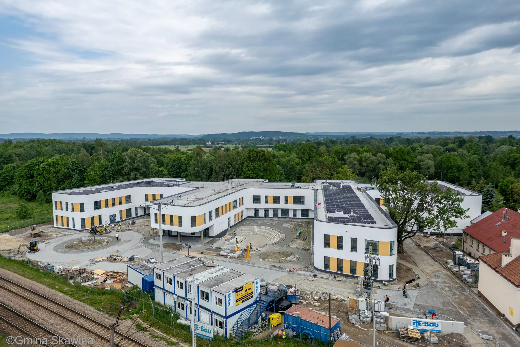 Gotowy kompleks Centrum Edukacyjnego w otoczeniu zieleni, dachy z panelami słonecznymi.